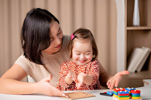 Woman watches and guides a young girl as they play with colorful building blocks on a table.